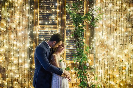 capa post: noivos abraçado em frente a parede com fairy light em casamento a noite