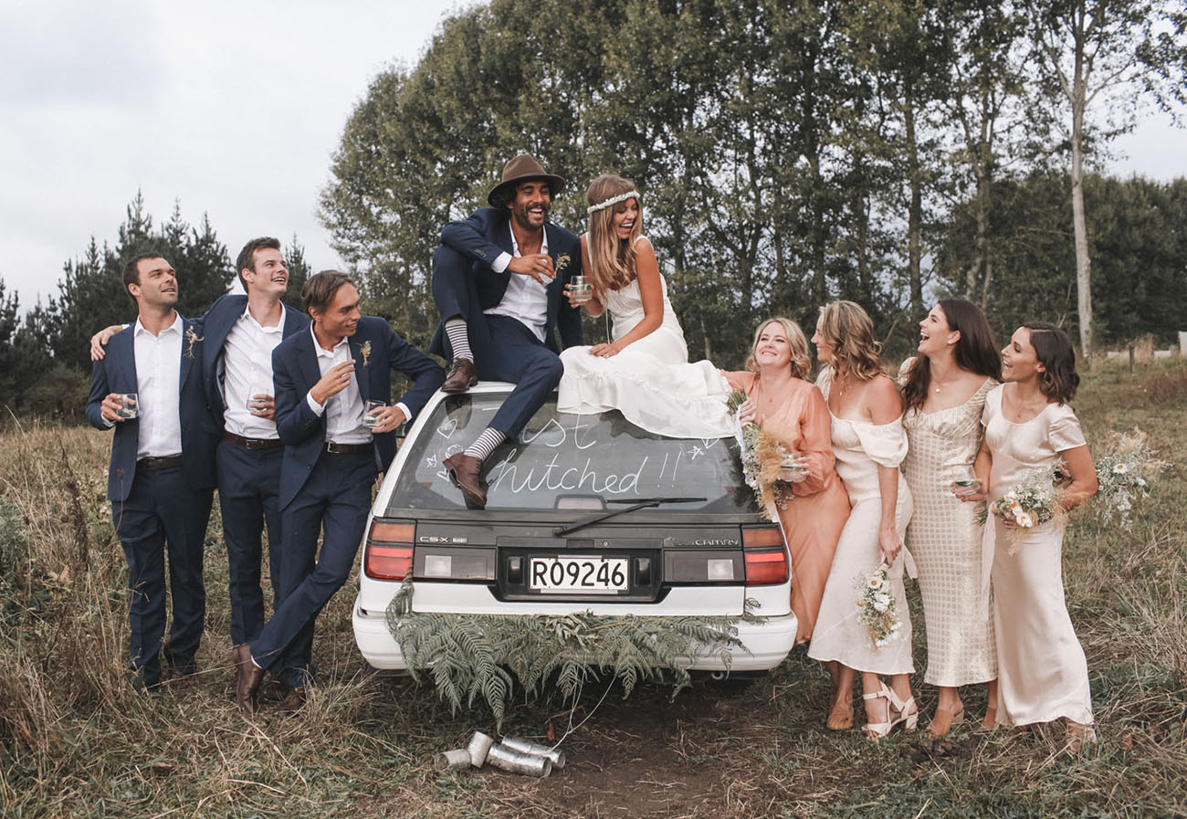 noivos em cima do carro com padrinhos e madrinhas celebrando um casamento no campo