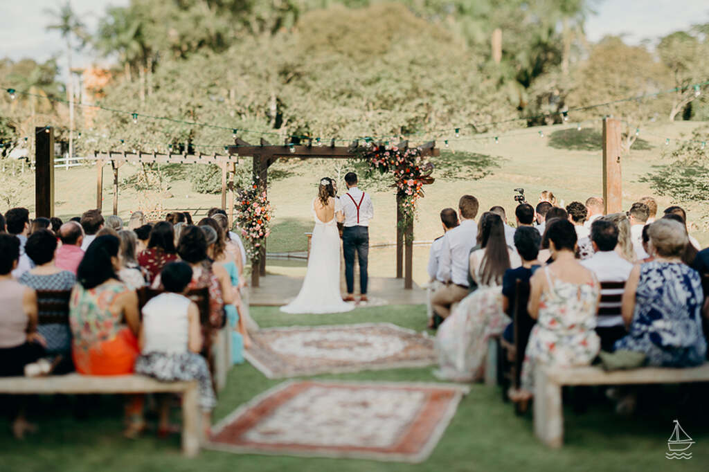 cerimônia de mini wedding ao ar livre com tapetes no caminho dos noivos e bancos de madeira para os convidados 