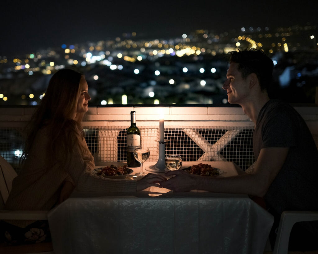 casal jantando na mesa na sacada com vista para a cidade iluminada