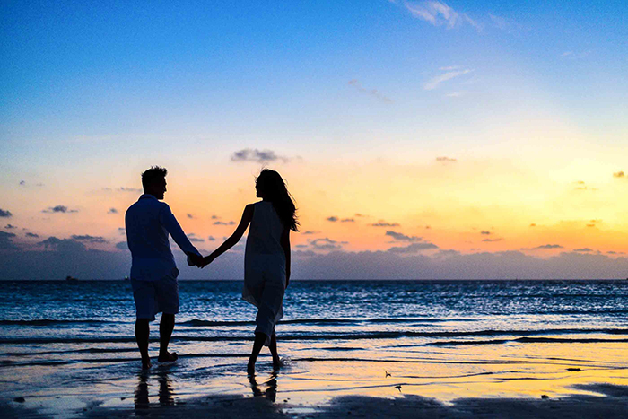 casal de mãos dadas caminhando na praia em lua de mel