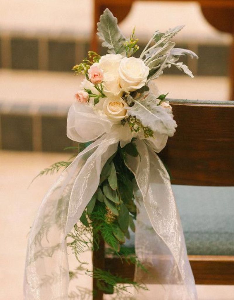 casamento na igreja com bancos decorados com arranjos de flores com cetim