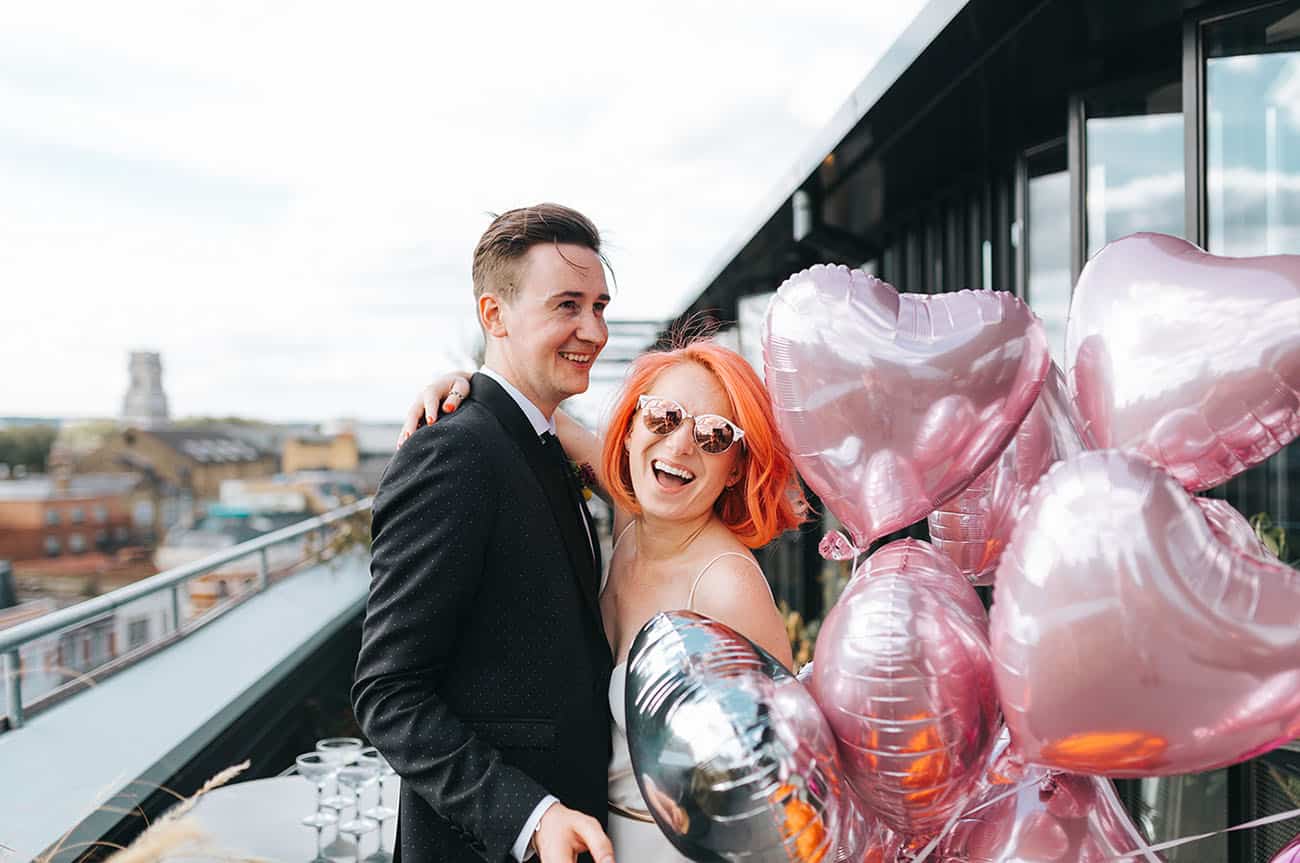 noivos sorrindo com balões de coração em micro wedding na cidade