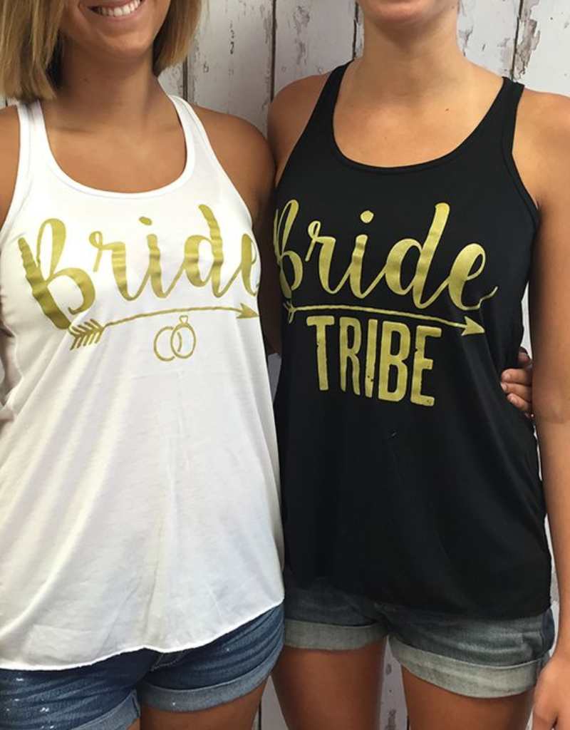 duas mulheres brancas usando camisetas regata. Uma veste camiseta regata branca e a outra preta. Ambas com escritos dourado "bride tribe"