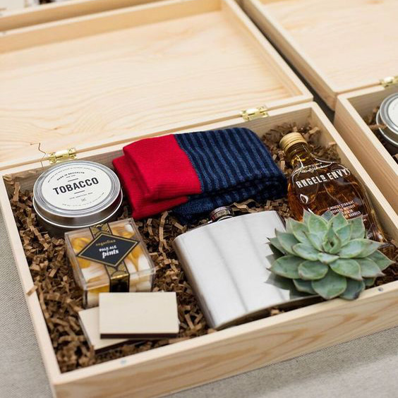 caixa de madeira com presentes para padrinho de casamento: suculenta, garrafa de bebida, cantil de aluminio, meia, lata com tabaco, fósforo e caixa com amêndoas.