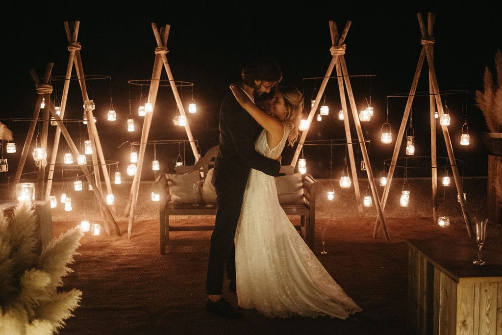 noivos abraçados com tendas com luminárias em casamento boho a noite