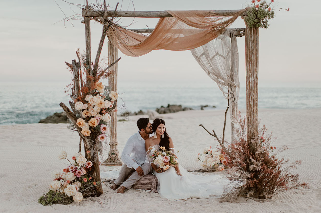 pergolado de madeira com noivos sentado em casamento boho na praia