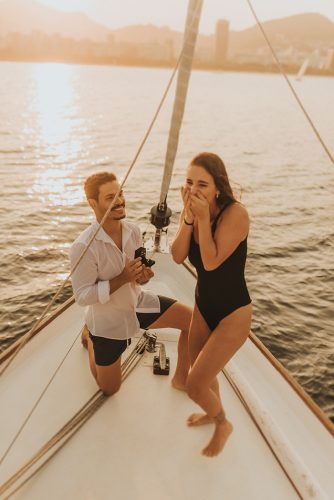 noivo ajoelhado no barco em alto mar para pedir namorada em casamento