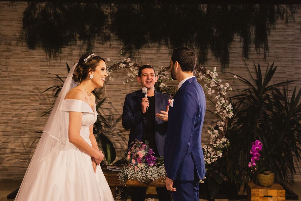casal de noivos durante cerimônia noturna em frente ao altar rindo com as palavras do celebrante de casamento