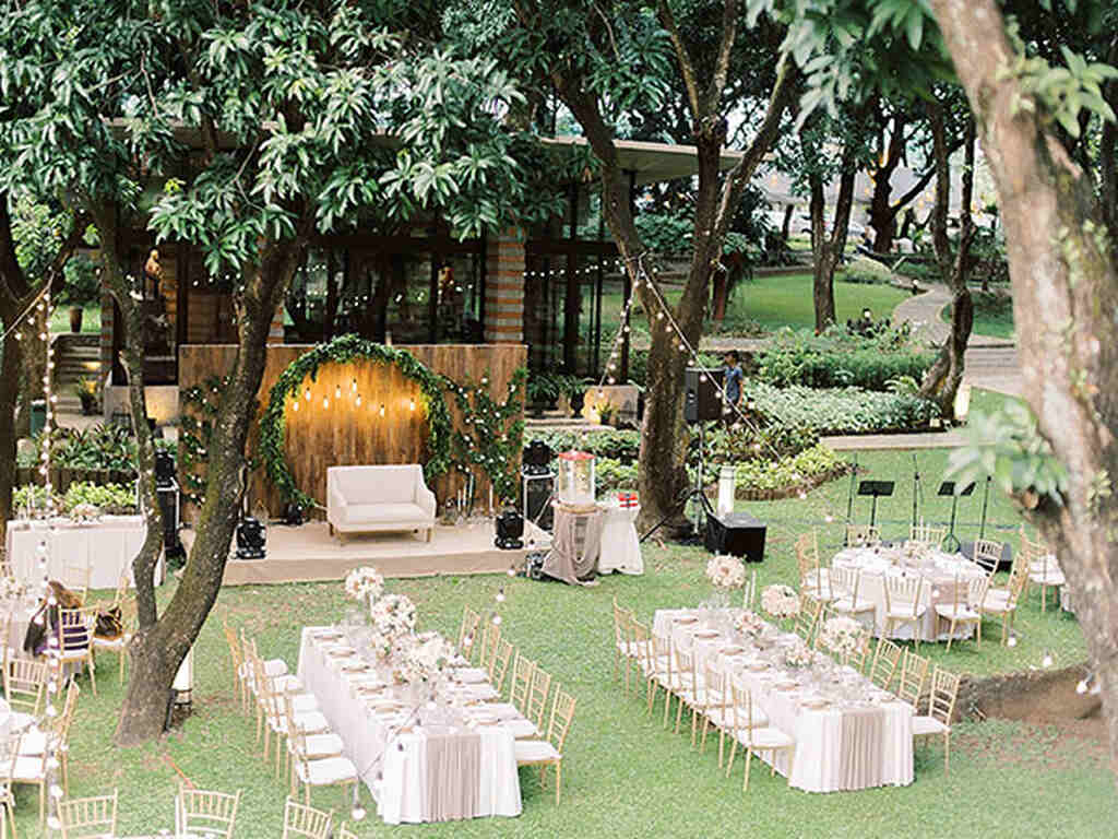 casamento no jardim com mesas comunitárias e uma poltorna para os noivos ao centro