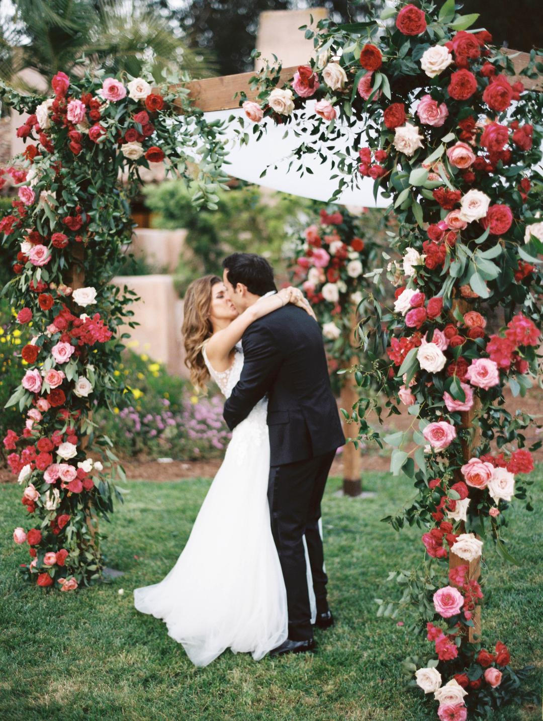 arco florido e noivos se beijando em casamento no jardim