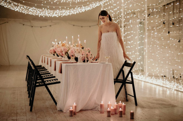 Noiva sentando em mesa cercada por varal de luzes em casamento minimalista