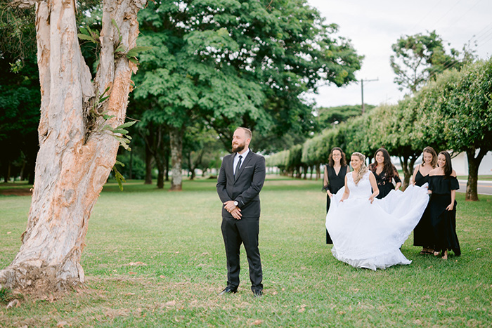 Noivo de pé e mulheres carregando vestido da noiva