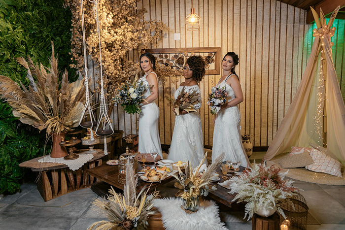 três noivas com buquês posando atrás de mesa com comidas