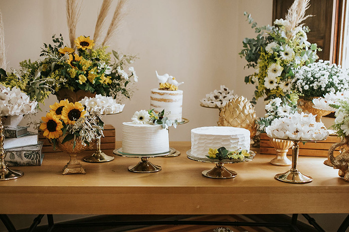 Mesa com flores brancas e amarelas e bolos
