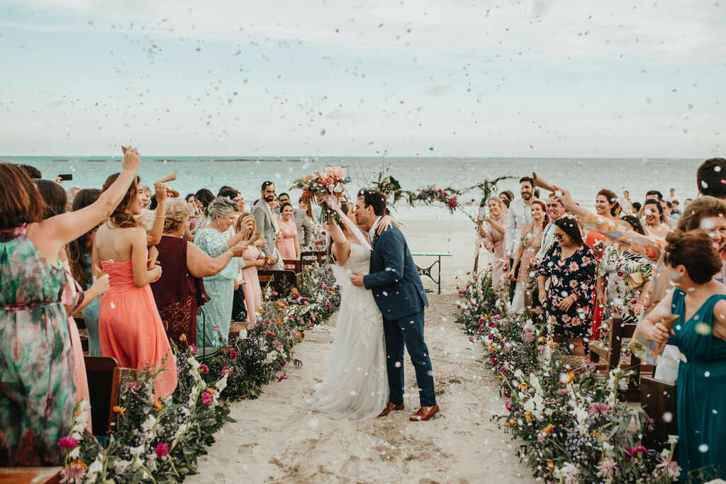 noivos se beijando na cerimônia de casamento na praia e convidados jogando pétalas de rosas 