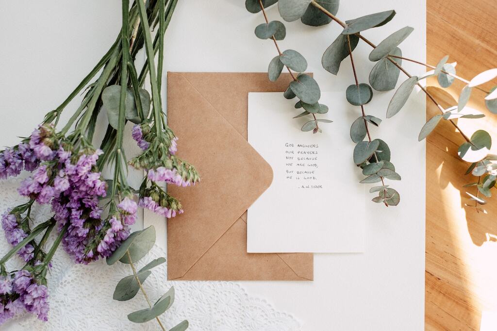 mini buquê com flores liláses e ramos de folhas de eucalipto sobre envelope com papel pardo e carta branca