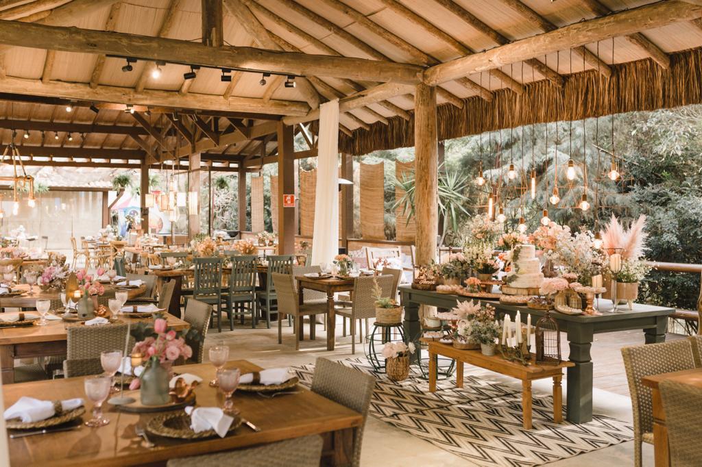 Salão com mesas decoradas com flores e capim dos pampas