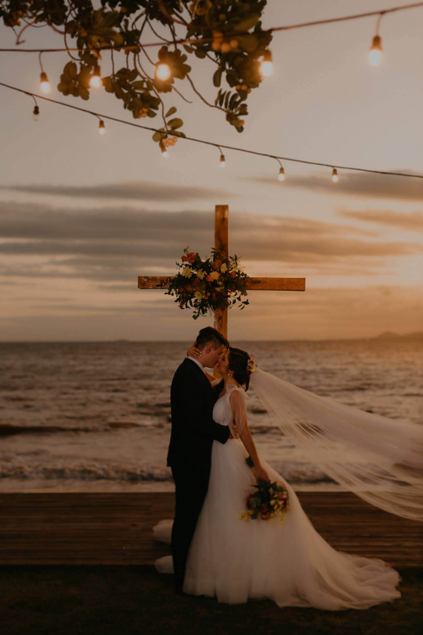 capa post: Noivos se beijando em frente a cruz