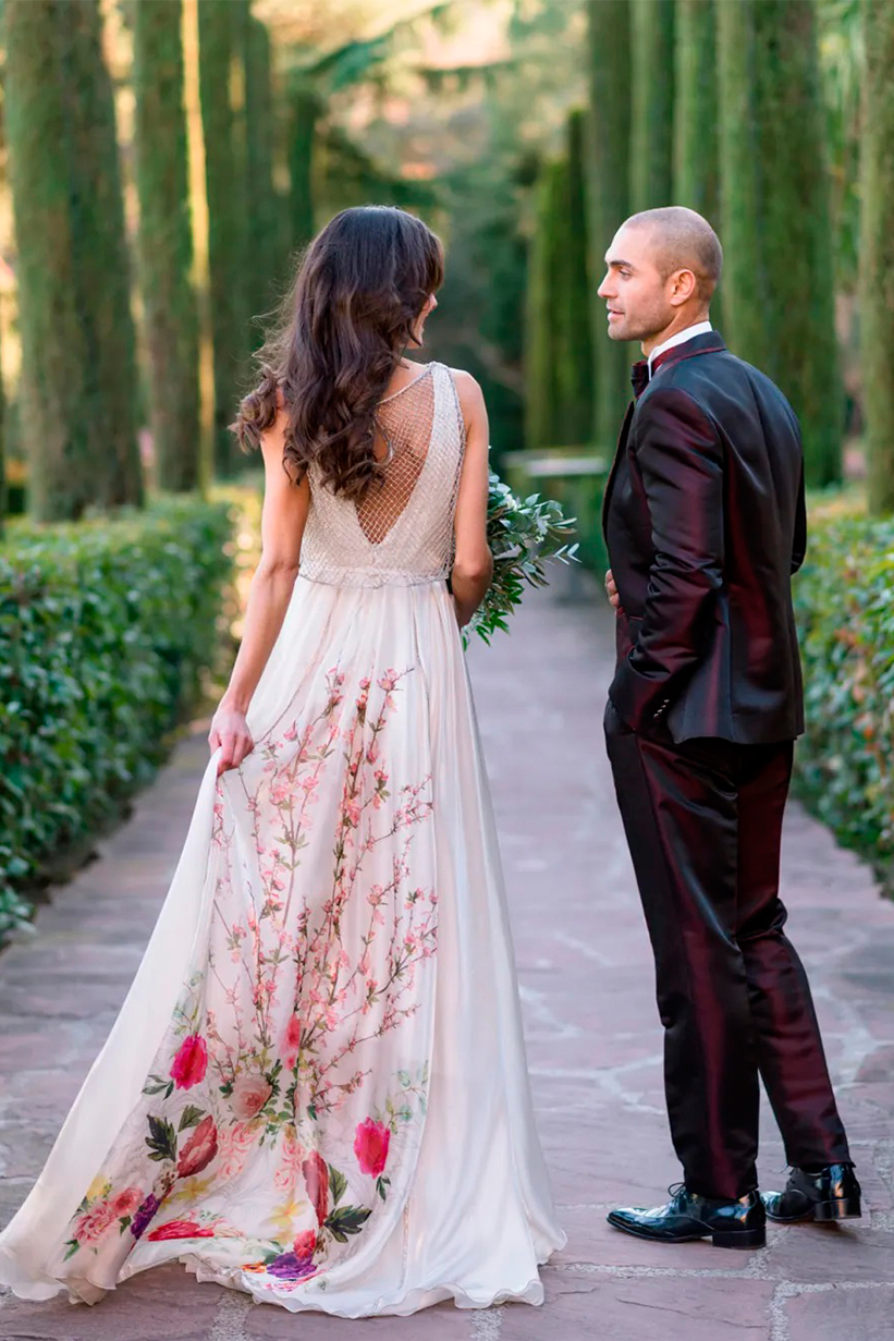 noivos caminhando com noivo de traje vinho e noiva com vestido florido
