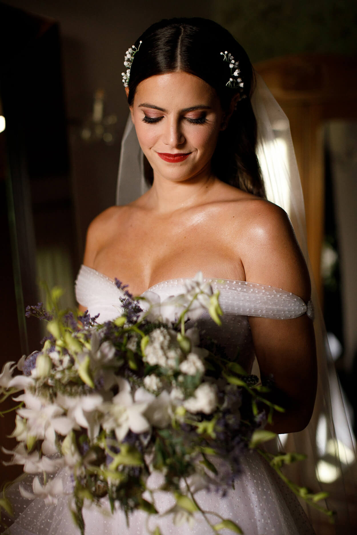 Mulher com vetsido de noiva com decote e alças nos ombos segurando buquê branco e lilás