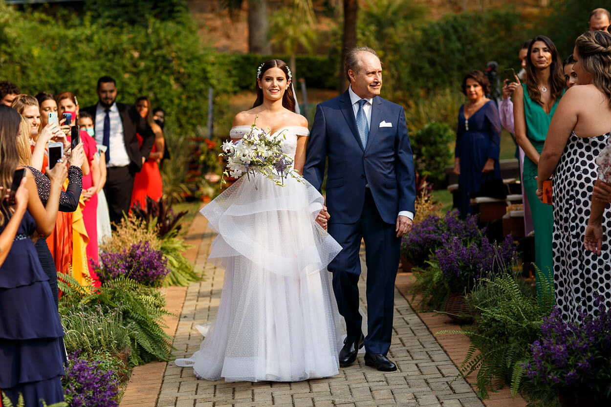 Noiva entrando no casamento com seu pai de terno azul escuro