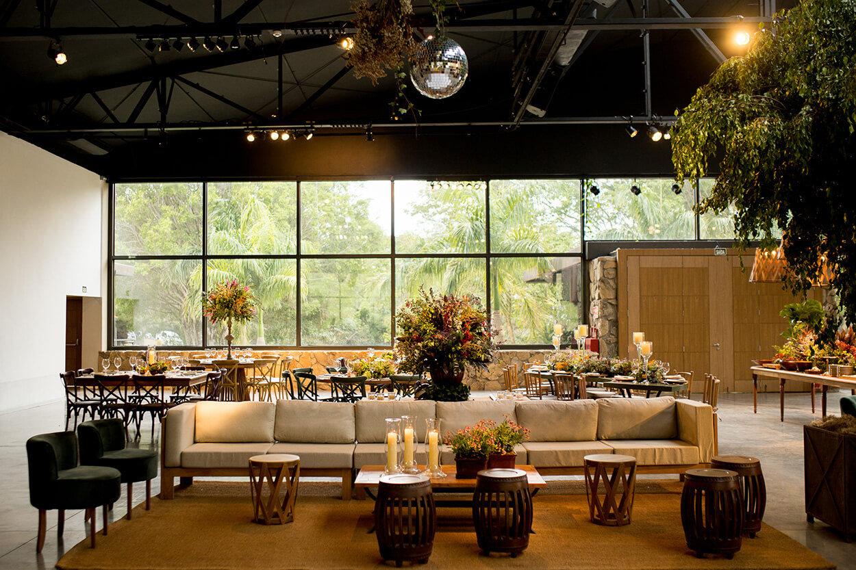 salão para festas com iluminação natural com sofá bege e mesas com flores