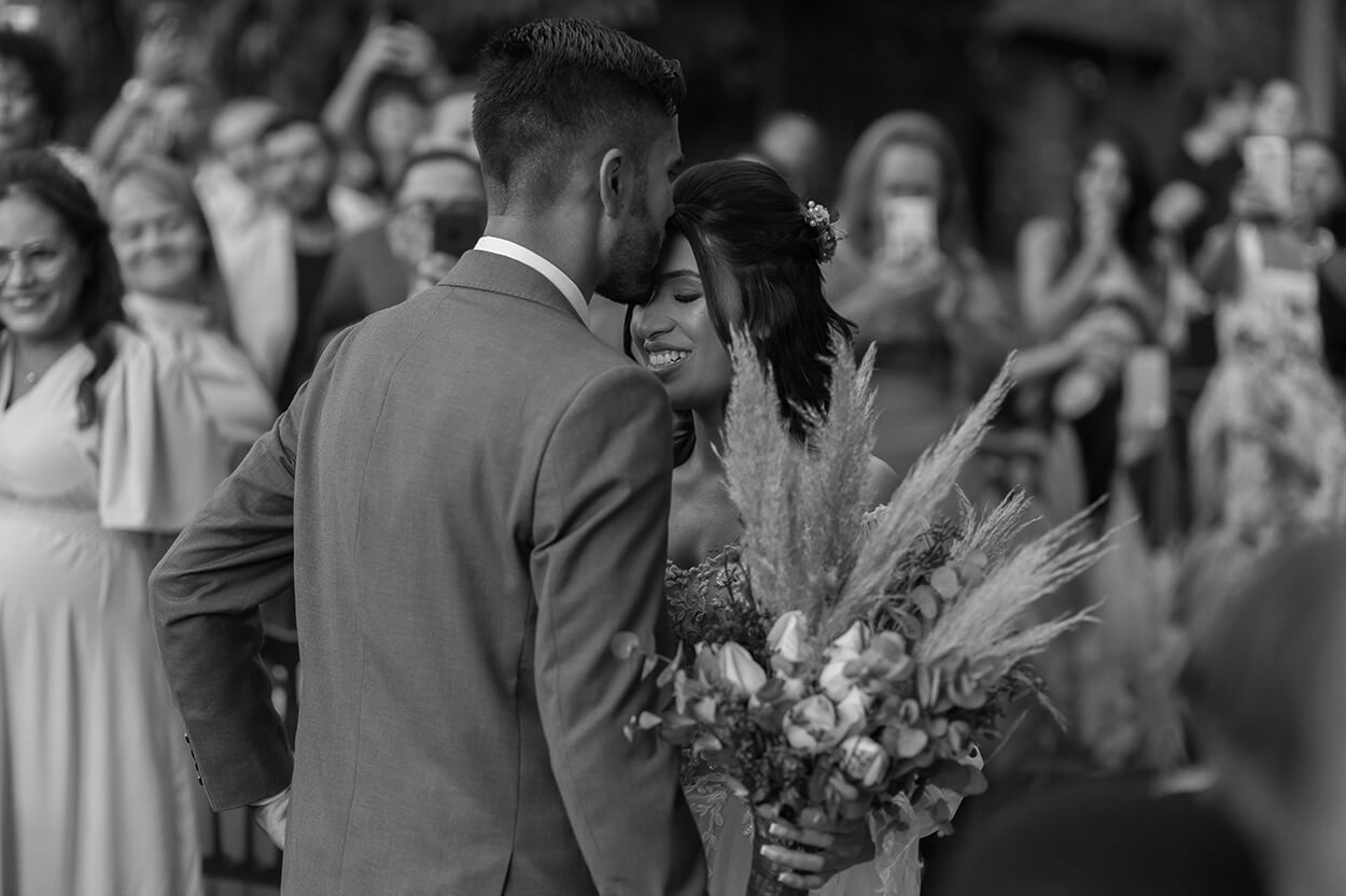 Foto em preto e branco do noivo beijando a testa da noiva