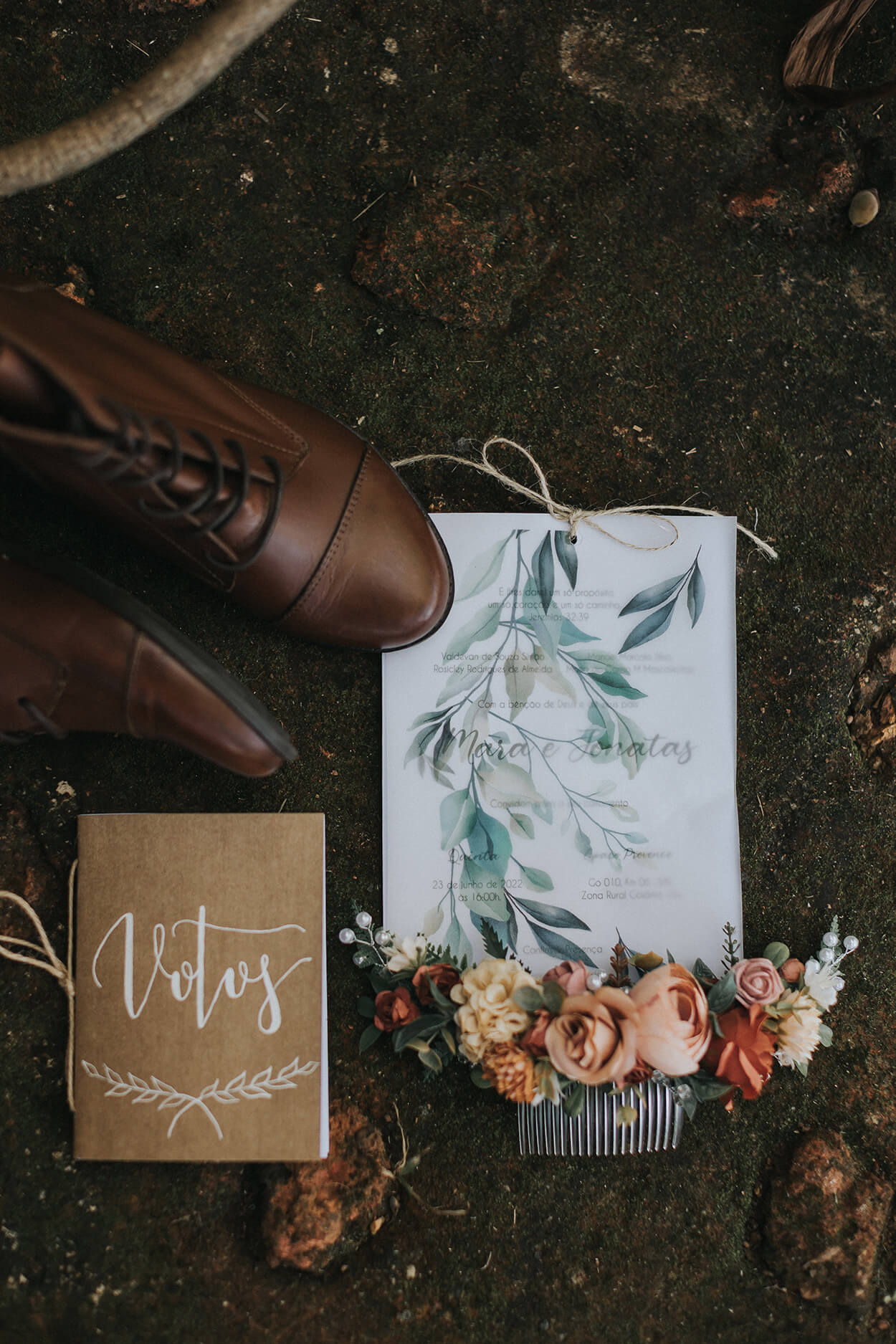 Bota marrom, caderno de votos com papel craft e letra delicada, pente para cabelo com flores decorativas e convite de casamento branco e azul com folhas