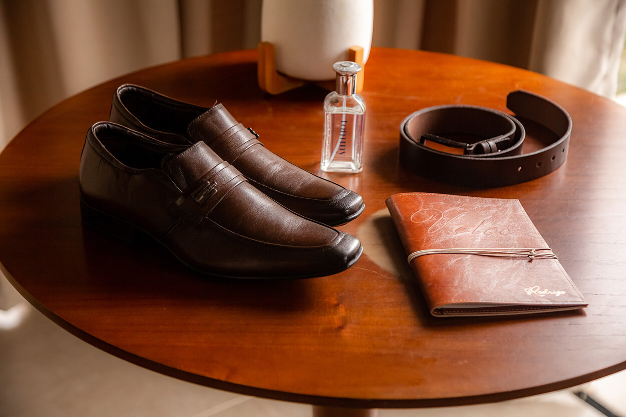 Sapato masculino, caderno marrom, perfume e cinto de couro sob a mesa de madeira