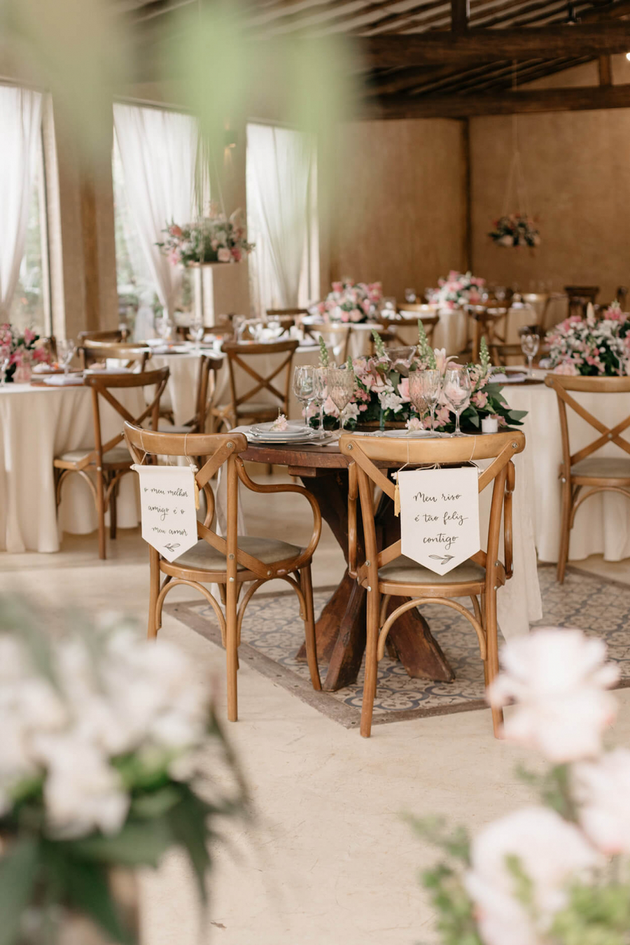 Salão com mesas redondas e decoradas com flores brancas e rosas