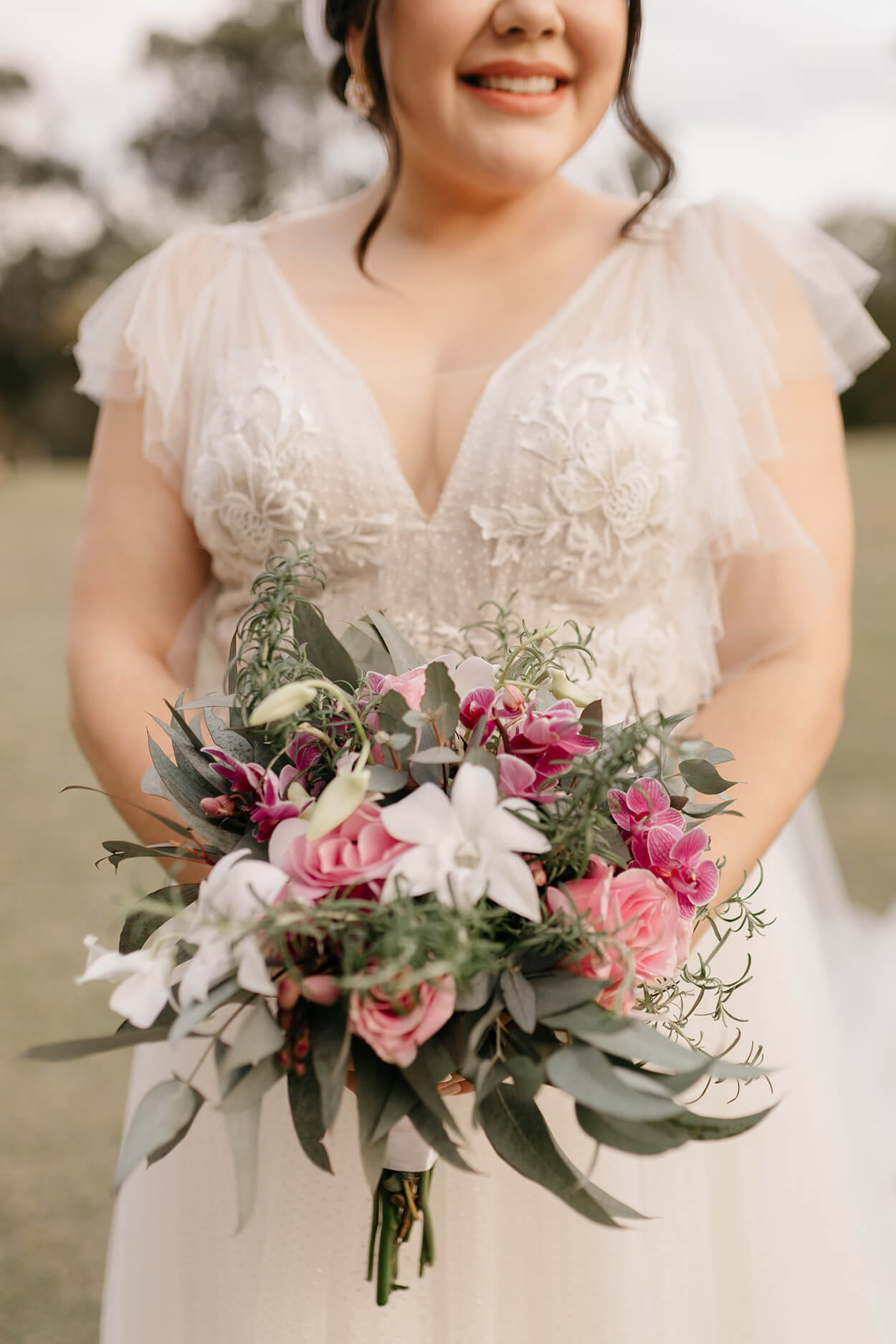 Noiva sorrindo segurando um buquê com flores brancas, rosas escuras e rosas cor de rosa