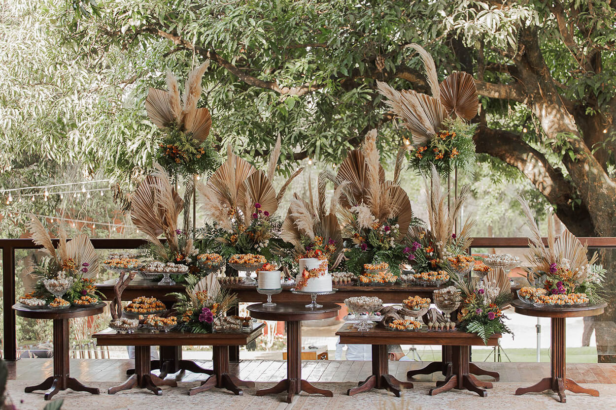 Mesas de madeira com dois bolos de casamento branco e flores laranjas com folhas secas