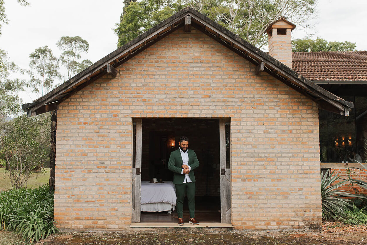 Noivo com terno verde na porta de casa antiga de tijolinhos