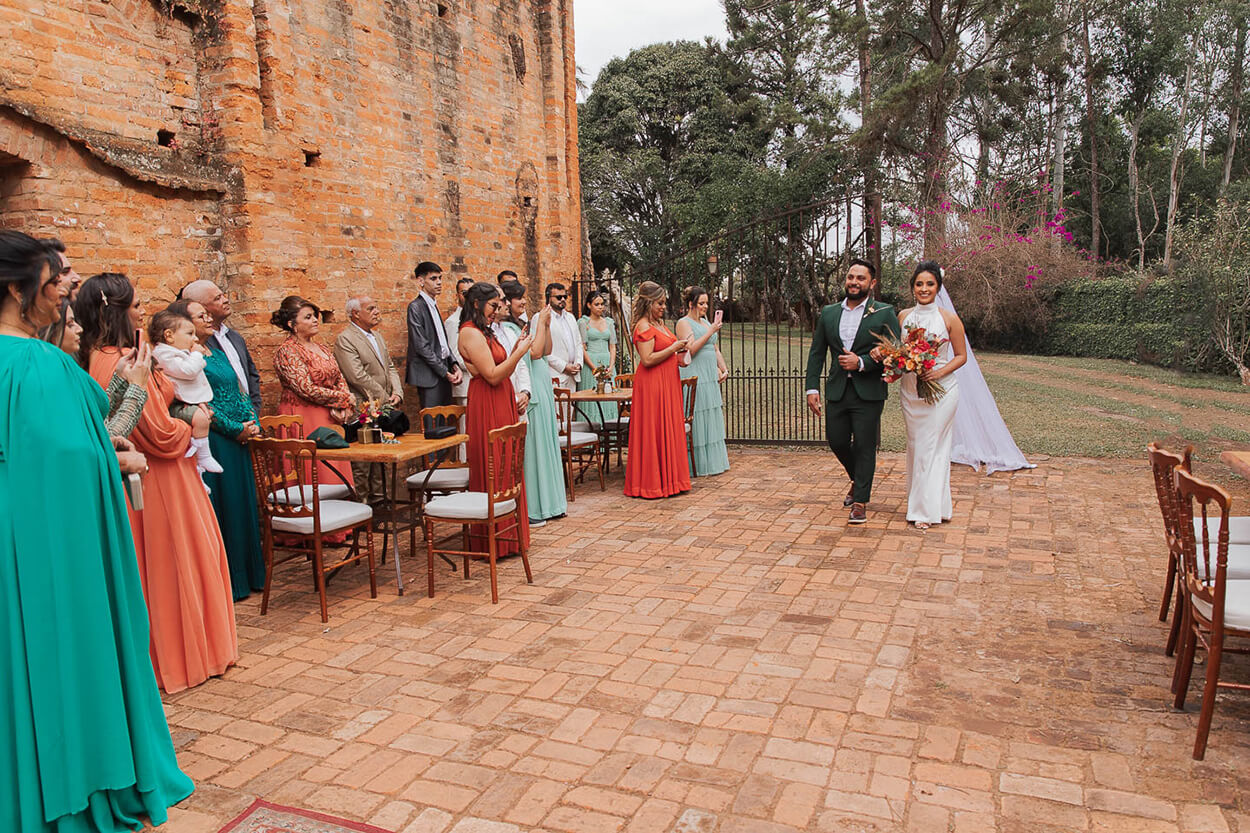 Convidados com roupas coloridas aplaudindo os noivos entrando no jardim