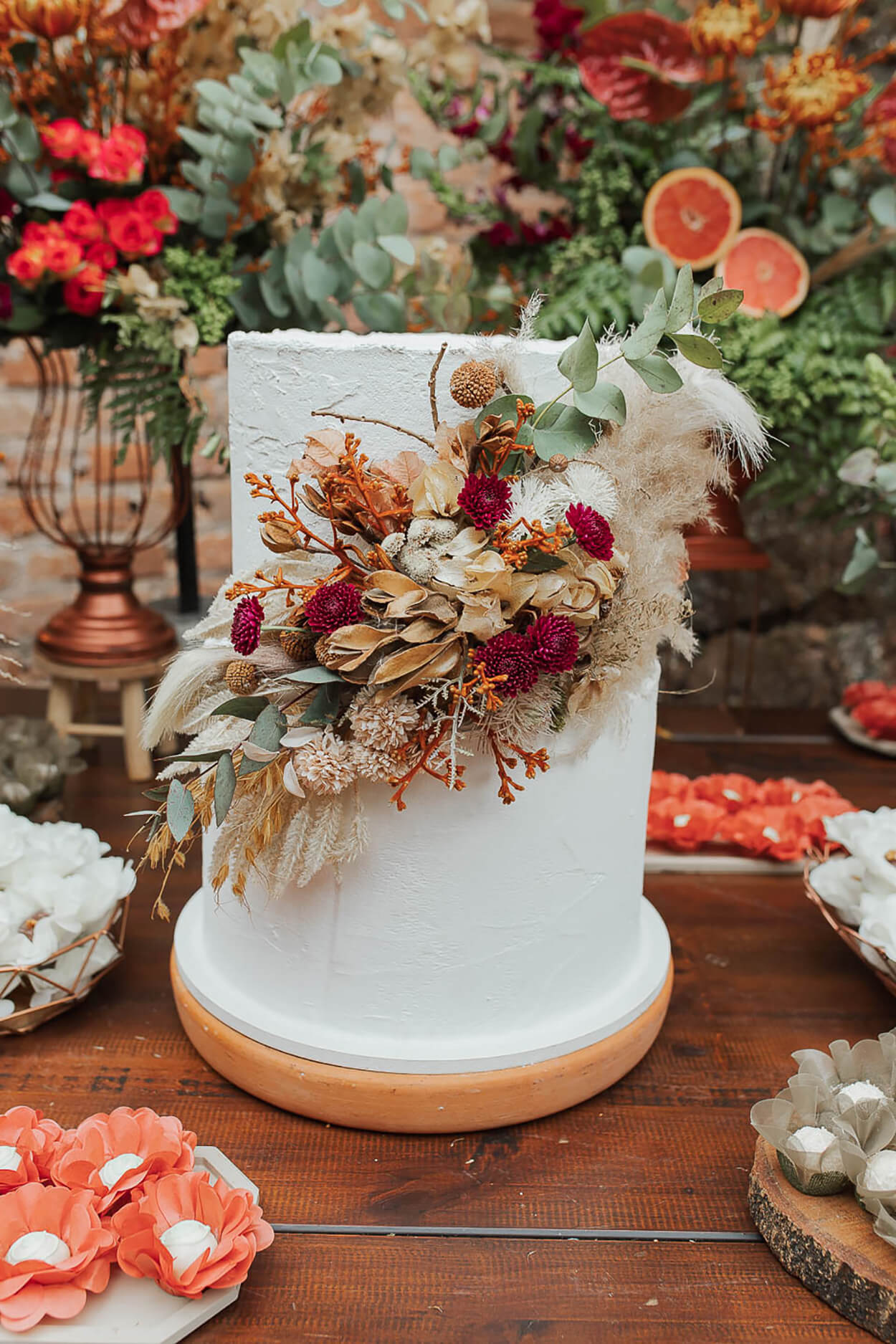 Bolo de casamento branco com dois andares com topo de bolo com flores laranjas, roxas e capim dos pampas