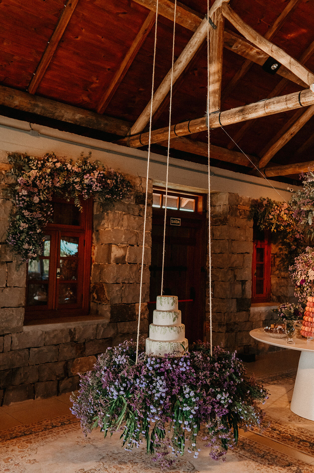 Mesa suspensa com flores lilás e bolo de casamento branco