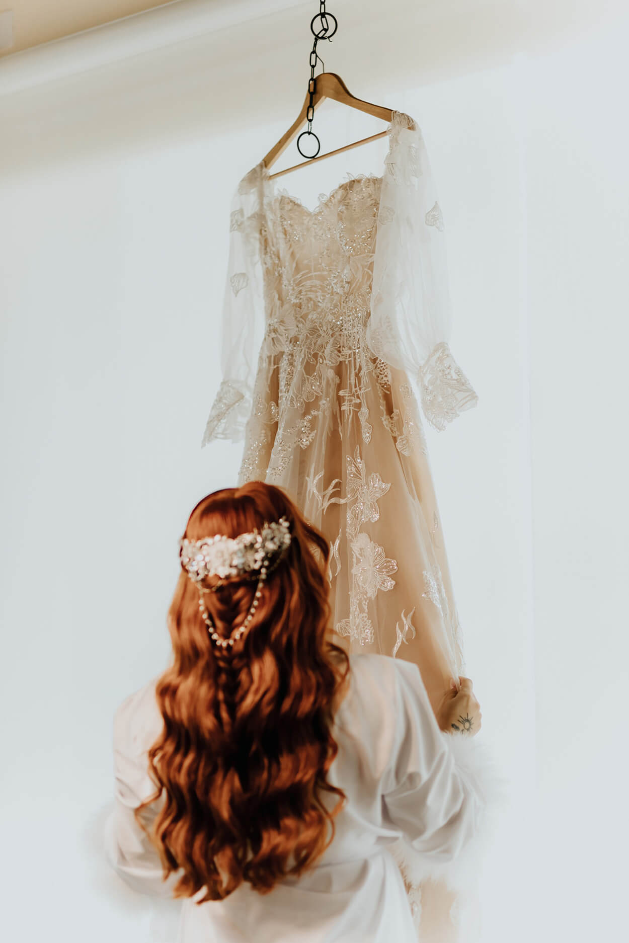 Mulher ruiva com cabelos longos com acessório de cabelo floral admirando seu vestido de noiva