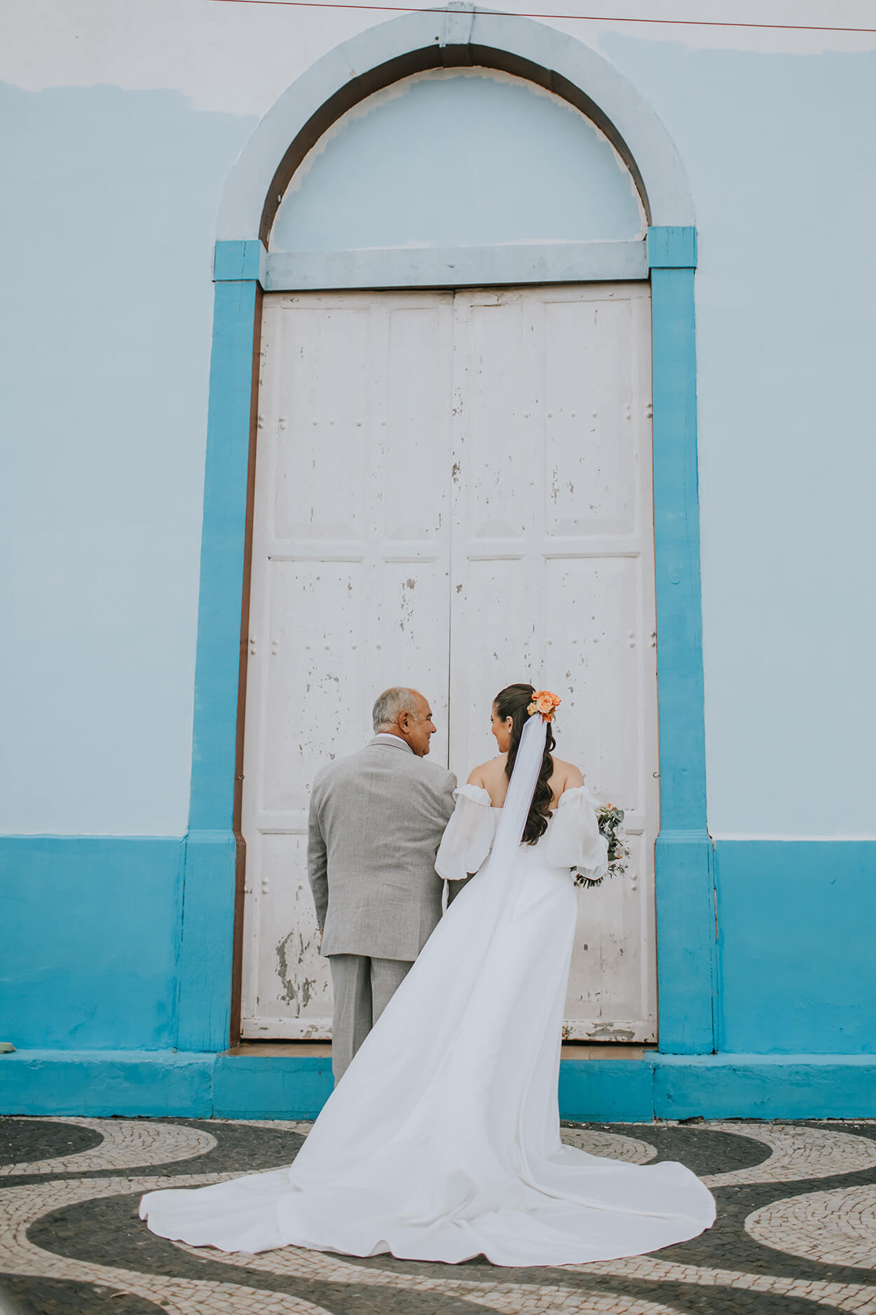 Noiva com sue pai de terno cinza aguardando a porta da igreja se abrir