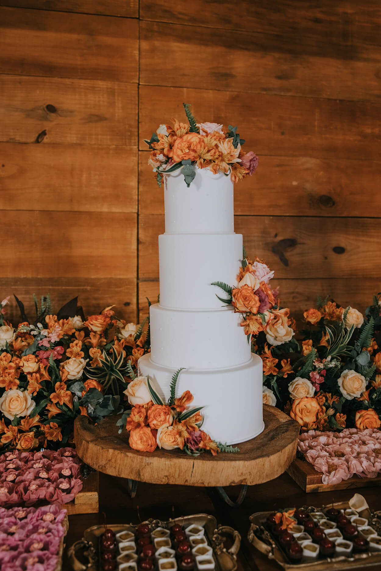 Bolo de casamento branco com quatro andares e com topo de rosas cor de rosa, claras e laranjas