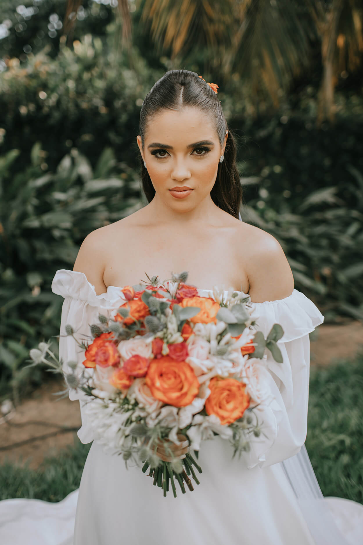 Mulher com vestido de noiva sem alças segurando buquê com rosas cor de rosa e laranjas