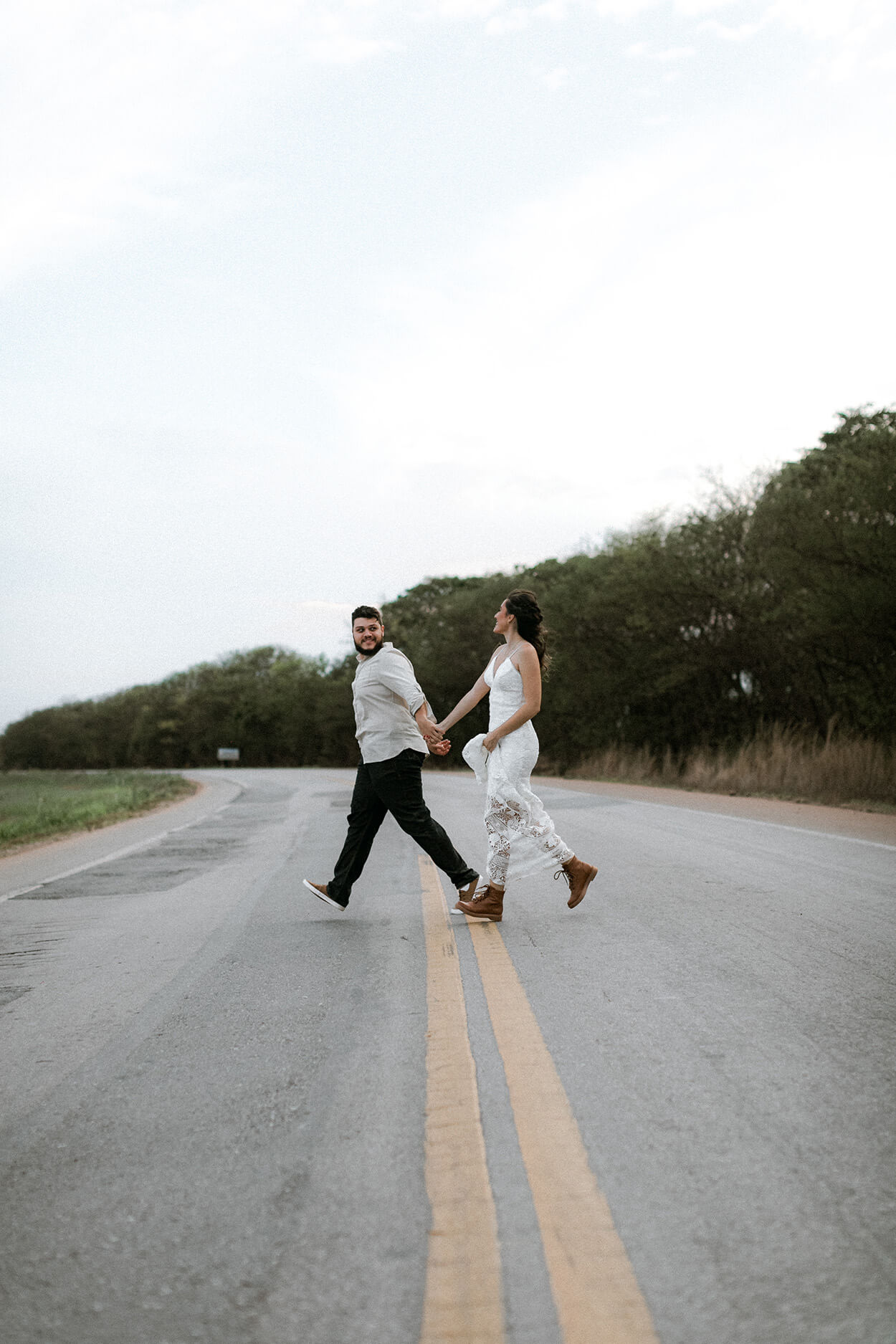 Casal de mãos dadas atravessando a estrada em um dia nublado