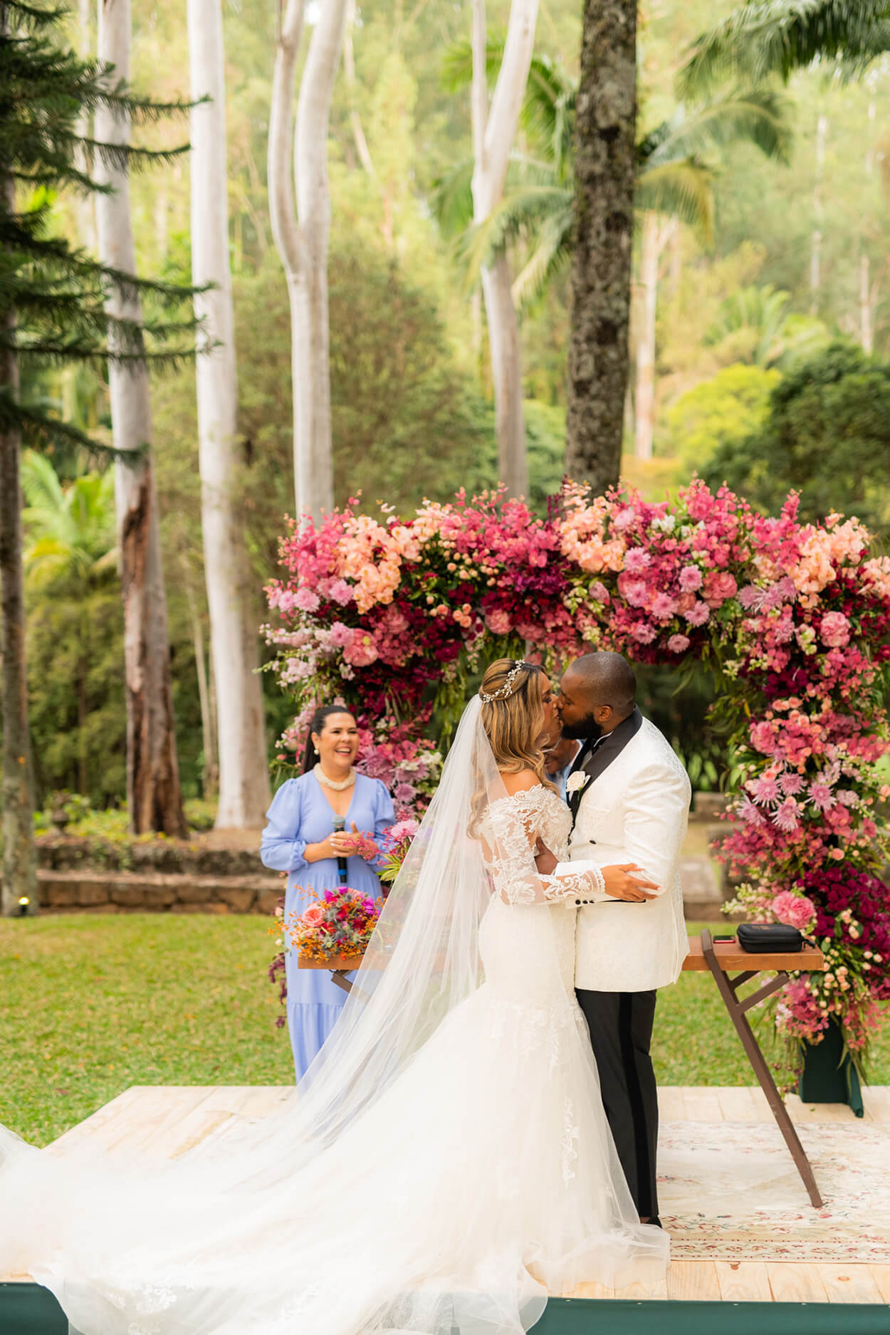 Noivos se beijando em frente a altar com flores rosas claras e vibrantes