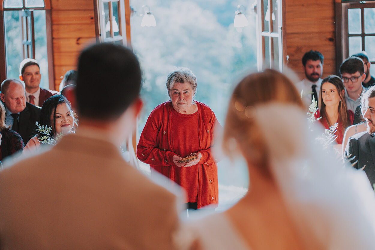 Avó do noivo com blusa laranja levando o porta alianças até o altar