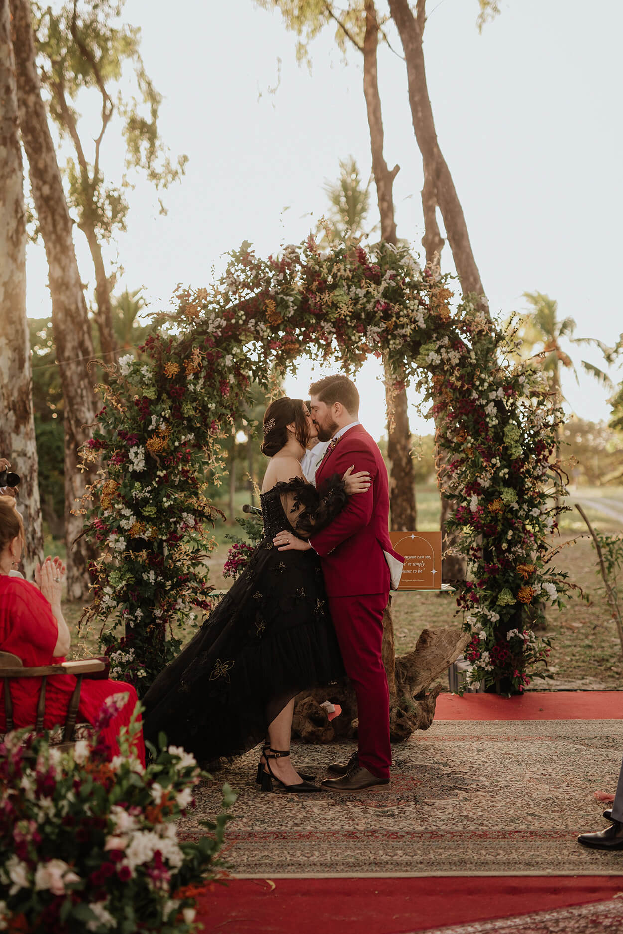 Noiva com vetsido preto beijando noivo com terno vermelho