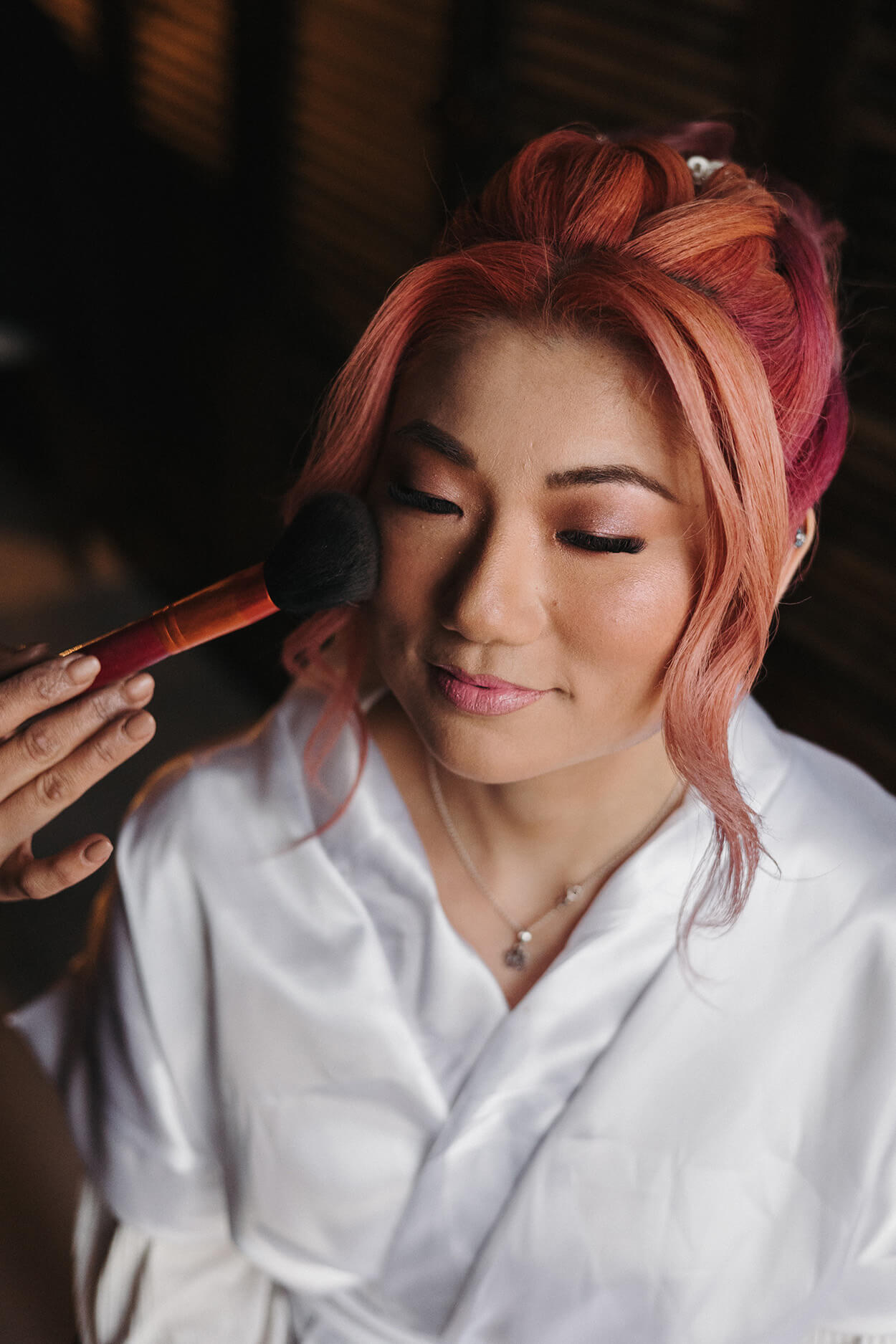 Mulher asiatica com cabelo rosa sendo maquiada