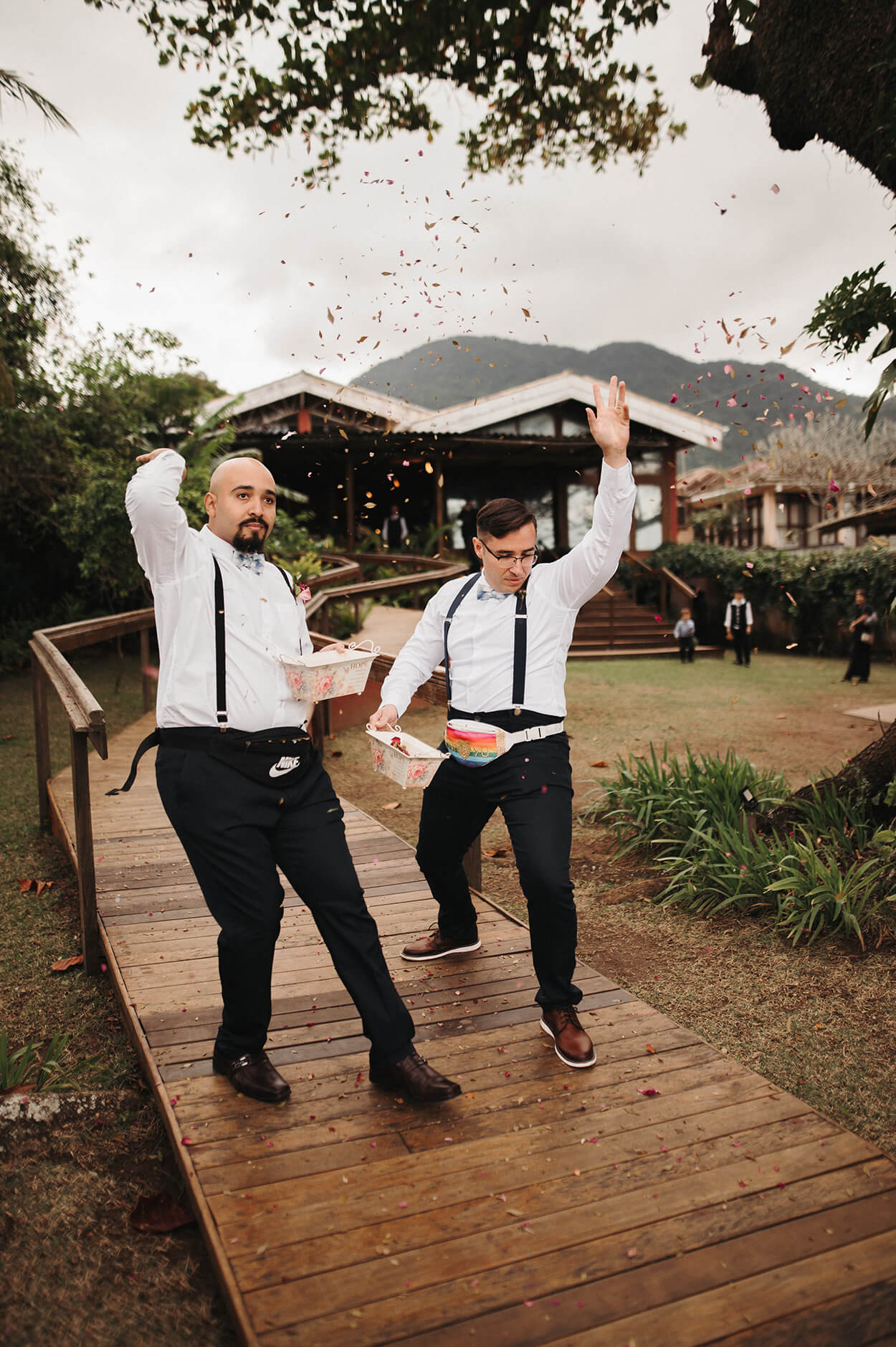 Dois homens como floristas do casamento. Eles usam calças preta e suspensórios jogando flores na entrada do casamento