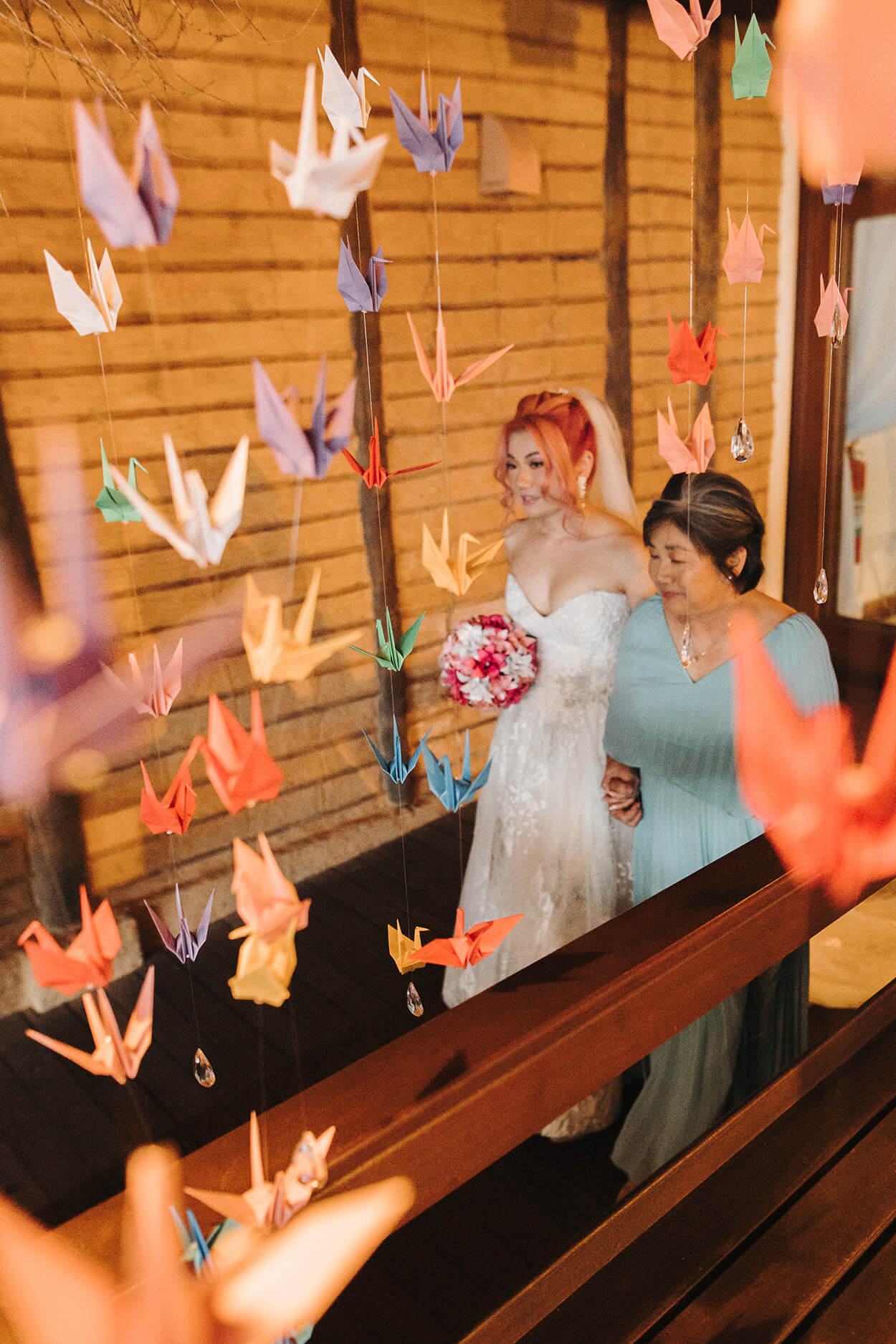 Noiva passando por um corredor com cortina de tsurus com a sua mãe de vestido azul claro