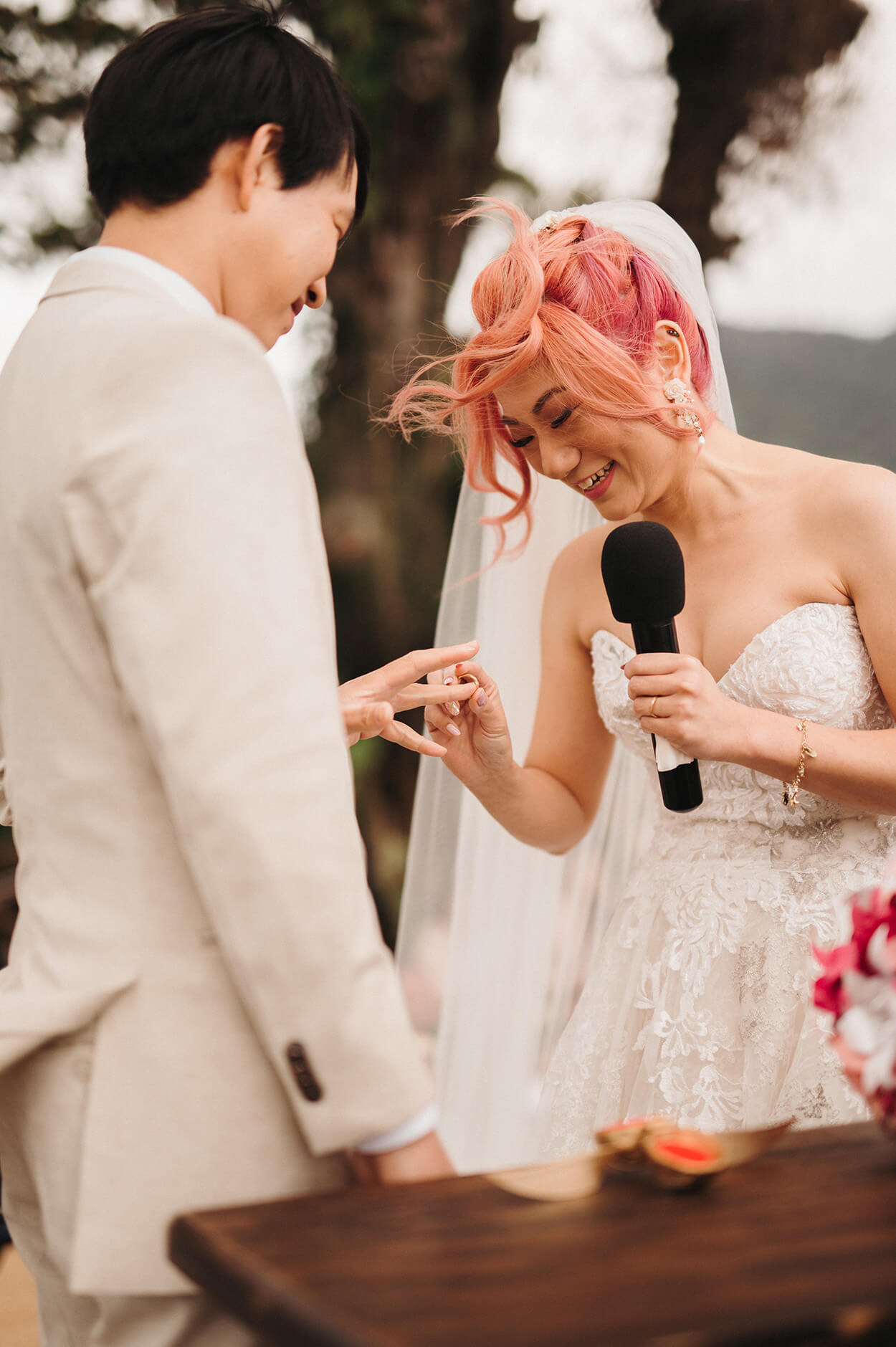 Noiva com cabelo rosa colocando aliança na mão do noivo