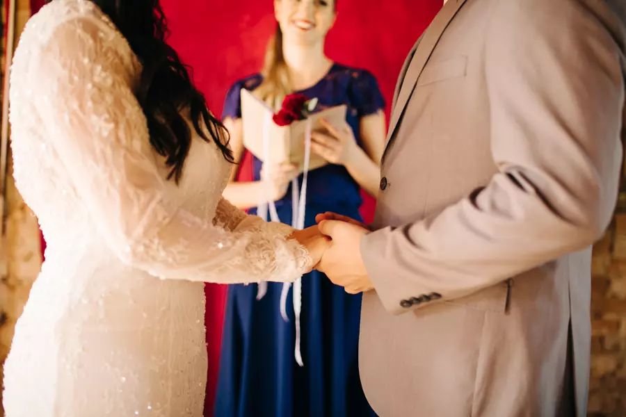 Noivos de mãos dadas em frente a celebrante de casamento durante a cerimônia